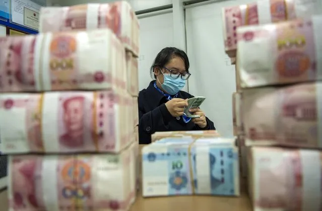 A clerk counts renminbi banknotes at a bank outlet in Hai'an city in eastern China's Jiangsu province,  Monday, December 6, 2021 China's central bank is trying to restrain the rise of the yuan after the currency hit a 2 1/2-year high against the dollar. (Photo by Chinatopix via AP Photo)
