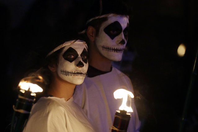 In this photo taken on Saturday, February 25, 2017 a couple watches the Torch Parade on the Greek island of Naxos. Almost 2,000 people took part in the procession of young men and women with faces painted to resemble black-and-white masks wear white sheets and hold torches on long poles. (Photo by Thanassis Stavrakis/AP Photo)