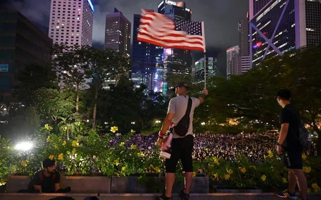A man holds up a US flag in front of a rally organised by Hong Kong mothers in support of extradition law protesters, in Hong Kong on July 5, 2019. A Hong Kong street artist was charged on July 5 with assaulting a police officer and criminal damage, the first prosecution against an anti-government protester since the city was rocked by unprecedented demonstrations. (Photo by Hector Retamal/AFP Photo)