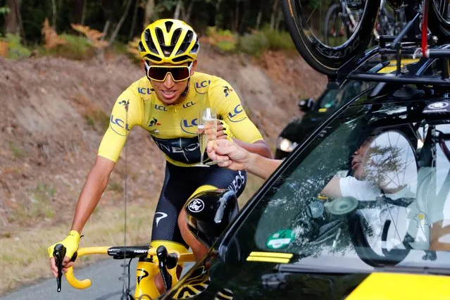 Colombia's Egan Bernal wearing the overall leader's yellow jersey drinks champagne at the car of his team director during the twenty-first stage of the Tour de France cycling race over 128 kilometers (79,53miles) with start in Rambouillet and finish in Paris, France, Sunday, July 28, 2019. (Photo by Thibault Camus/AP Photo)