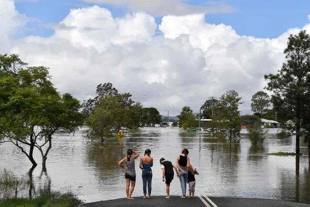 A family stays next to a flooded street in Lawrence, some 70 kms from the New South Wales town of Lismore, Australia on March 1, 2022. (Photo by Saeed Khan/AFP Photo)
