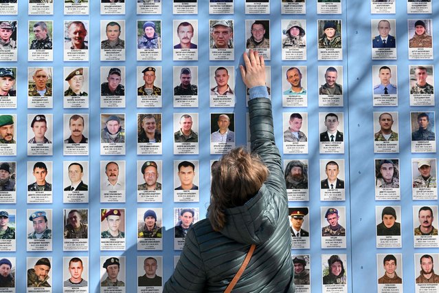 A woman touches a picture of her died son at Memory Wall of Fallen defenders of Ukraine in the Russian-Ukrainian War during a ceremony marking the Day of Volunteer in Kyiv on March 14, 2023. (Photo by Sergei Supinsky/AFP Photo)