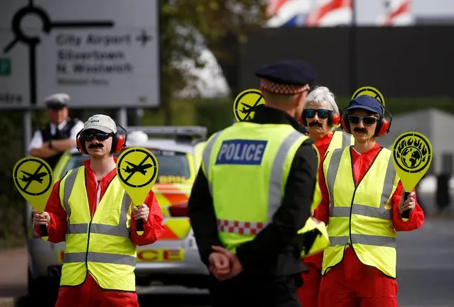 Extinction Rebellion protesters dressed as airport marshalls block the road during a demonstration, near London City Airport, in London, Britain, October 10, 2019. Some hundreds of climate change activists are in London during a fourth day of world protests by the Extinction Rebellion movement to demand more urgent actions to counter global warming. (Photo by Henry Nicholls/Reuters)