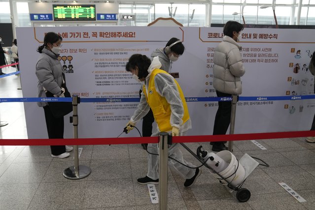 A woman wearing protective gear sprays disinfectant as a precaution against the coronavirus while people wait in line at a local polling station of the early voting for the March 9 presidential election in Seoul, South Korea on March 4, 2022. Tens of millions of South Koreans are expected to vote Wednesday, March 9 to choose their new president. The winner will take office on May 10 for a single five-year term. Whoever wins, a new leader will be tasked with resolving various economic woes, easing threats from nuclear-armed North Korea and healing a nation sharply split along the lines of ideology, generation and gender. (Photo by Lee Jin-man/AP Photo)