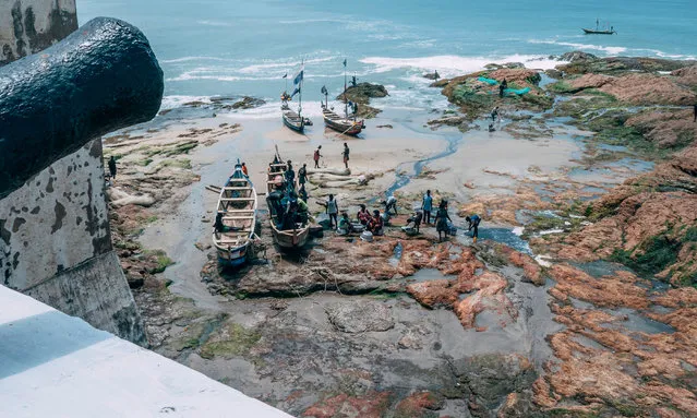Fishermen tend to their boats on the shores of Cape Coast Castle, Ghana on August 18, 2019. African-American visitors are flocking to Ghana as it marks the “Year of Return” to remember the 400th anniversary of the first slave ship landing in Virginia. The West African nation is banking on the commemorations to give a major boost to the number of tourist arrivals as it encourages the descendants of slaves to “come home”. Cape Coast Castle, 150 kilometres (90 miles) from the capital Accra, is a major magnet for those visiting. The white-washed fort lined with cannons was one of dozens of prisons studding the Atlantic coast where slaves were held before their journey to the New World. (Photo by Natalija Gormalova/AFP Photo)