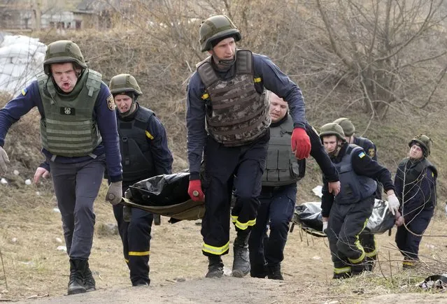 Ukrainian soldiers carry bodies of civilians killed by the Russian forces over the destroyed bridge in Irpin close to Kyiv, Ukraine, Thursday, March 31, 2022. The more than month-old war has killed thousands and driven more than 10 million Ukrainians from their homes including almost 4 million from their country. (Photo by Efrem Lukatsky/AP Photo)
