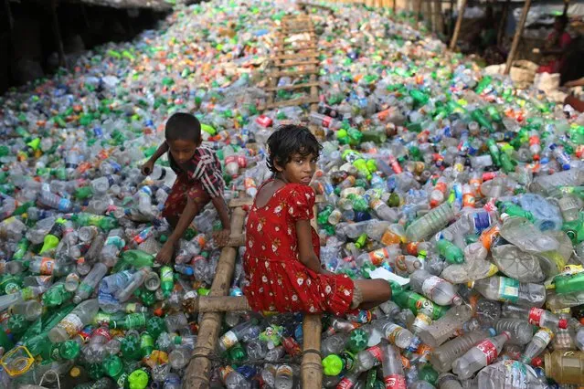 Bangladeshi girl Sharmin, 13 years old, looks into the camera as she works at a plastic recycling factory as a boy plays on a heap of bottles in Dhaka, Bangladesh, Thursday, June 12, 2014. June 12 marks the “World Day Against Child Labor”, that was initiated in 2002 by the International Labor Organization to highlight the plight of child workers across the world. (Photo by A.M. Ahad/AP Photo)