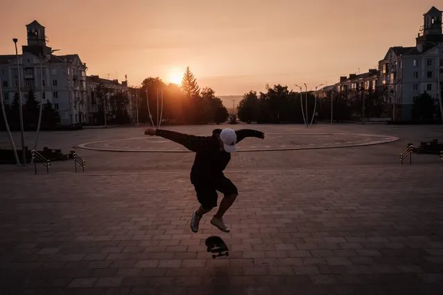 Roman Kovalenko, 18, practices the skate trick at sunset as he always skates alone since all his friends have fled at Peace Square in Kramatorsk, eastern Ukraine, on May 5, 2022, amid the Russian invasion of Ukraine. (Photo by Yasuyoshi Chiba/AFP Photo)