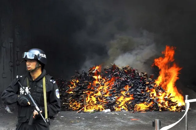 A police officer stands guard over a pile of firearms burning during a ceremony to destroy illegal weapons in Yuxi, China on June 12, 2012