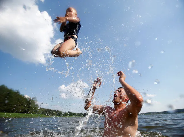 A man with a boy cool themselves down in a lake as the temperature reaches up to 35 degrees Celsius (95 degrees Fahrenheit) near the village of Novosyolki, Belarus, June 25, 2016. (Photo by Vasily Fedosenko/Reuters)