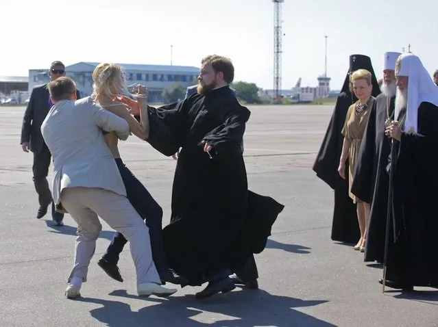 A topless protester from the Ukrainian feminist group Femen is blocked by a security guard and a priest as she tries to throw herself at the leader of the Russian Orthodox Church