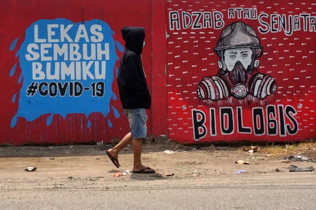 An Indonesian man wearing a face mask walks past murals amid concerns of the COVID-19 coronavirus outbreak in Tangerang on March 29, 2020. Indonesia as of March 28 has declared 1,155 confirmed infections with 102 deaths, making it the country with the highest fatality rate in Southeast Asia. (Photo by Fajrin Raharjo/AFP Photo)