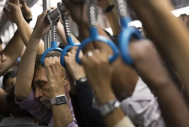 In this September 17, 2014, photo, a man closes his eyes as he stands with other commuters in a crowded metro car during rush hour in Rio de Janeiro. On packed subways and crowded highways, billions of people worldwide participate in a short-distance population shift twice a day: the rhythmic ritual of the daily commute to and from work. (Photo by Leo Correa/AP Photo)