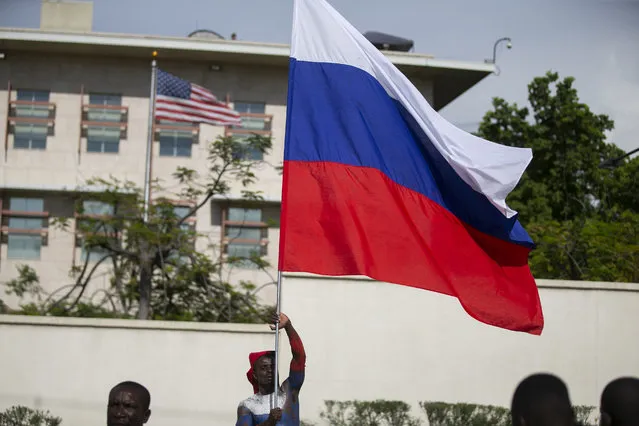 A man waves a Russian national flag in front of the U.S. embassy as he hopes for support from the Russian government, during a protest to reject an international military force requested by the government and to demand the resignation of Prime Minister Ariel Henry, in Port-au-Prince, Haiti, Monday, October 17, 2022. The United Nations Security Council is evaluating the request by the Haitian government for the immediate deployment of foreign troops to help free Haiti from the grip of gangs that has caused a scarcity of fuel, water and other basic supplies. (Photo by Joseph Odelyn/AP Photo)
