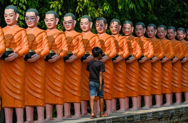 A boy walks past statues of Buddhist monks at Trapeang Thma pagoda in Cambodia's Banteay Meanchey province on March 24, 2025. (Photo by Tang Chhin Sothy/AFP Photo)