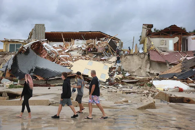 People look on at homes that are partially toppled onto the beach after Hurricane Nicole came ashore on November10, 2022 in Daytona Beach, Florida.  Nicole came ashore as a Category 1 hurricane before weakening to a tropical storm as it moved across the state. (Photo by Joe Raedle/Getty Images)