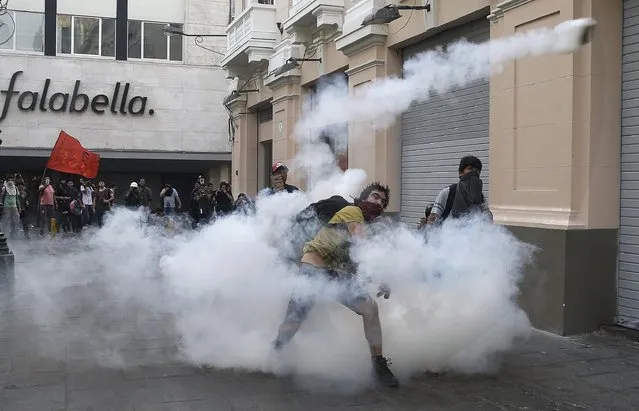 A demonstrators throws a tear gas canister back towards the police during clashes against the pardon of former President Alberto Fujimori in Lima, Peru, Monday, December 25, 2017. Peru's President Pedro Pablo Kuczynski announced Sunday night that he granted a medical pardon to the jailed former strongman who was serving a 25-year sentence for human rights abuses, corruption and the sanctioning of death squads. (Photo by Martin Mejia/AP Photo)