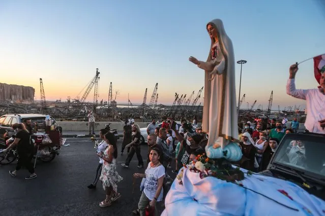 People gather in front of the devastated port of Beirut as a car carrying a statue of the Virgin Mary drives during a procession marking the day of the Assumption on August 15, 2020, more than a week after a massive chemical explosion disfigured the Lebanese capital. (Photo by AFP Photo/Stringer)