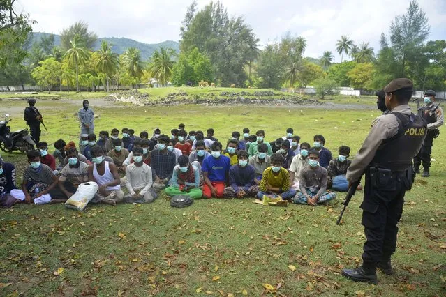 Indonesian police officers watch a group of ethnic Rohingya people after they landed on Indra Patra beach in Ladong village, Aceh province, Indonesia, Sunday, December 25, 2022. A wooden boat carrying dozens of Rohingya Muslims landed on the northern most province Sunday. (Photo by Rahmat Mirza/AP Photo)