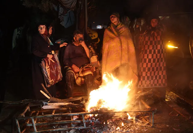 People warm themselves around a bonfire in the rubble in Kahramanmaras, Turkey, after a 7.8-magnitude earthquake struck the country's southeast on February 7, 2023. A major 7.8-magnitude earthquake struck Turkey and Syria, killing more than 3,000 people and flattening thousands of buildings as rescuers dug with bare hands for survivors. (Photo by Adem Altan/AFP Photo)