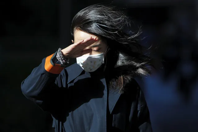 A woman wearing a face mask to help curb the spread of the coronavirus uses her hand to shield from the wind on a street in Beijing, Wednesday, October 21, 2020. (Photo by Andy Wong/AP Photo)