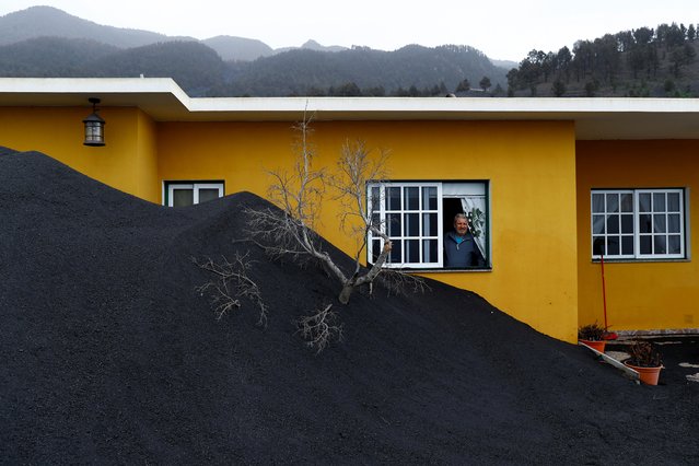 Dionisio Leal looks at heaps of ash from the Cumbre Vieja volcano surrounding his house as he stands at the window, in Las Manchas neighbourhood on the Canary Island of La Palma, Spain, January 20, 2022. (Photo by Borja Suarez/Reuters)