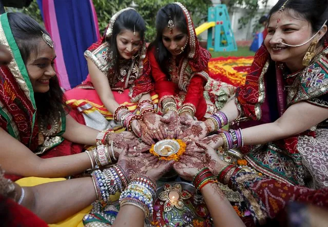 Women with their hands decorated with henna paste pose for pictures as they pray during the Hindu festival of Karva Chauth in Ahmedabad, India, October 30, 2015. (Photo by Amit Dave/Reuters)