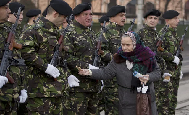 A woman offers biscuits to honor guard soldiers before a commemoration at the Revolution Heroes Cemetery in Bucharest ,Romania, Sunday, December 21, 2014. The anti-communist uprising, which left more than thousands dead, and ended the rule of dictator Nicolae Ceausescu, who was executed, started in the western Romanian town of Timisoara on Dec. 16, 1989 and in Bucharest, Romania's capital on Dec. 21, 1989. (Photo by Vadim Ghirda/AP Photo)
