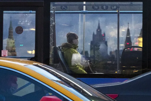 A woman wearing a face mask to protect against coronavirus, rides on a bus, with Kremlin's towers, left and right, and Russian Foreign Ministry building, center, in the background, in Moscow, Russia, Wednesday, December 23, 2020. Russia, which has so far registered more than 2.8 million confirmed cases of the virus and over 51,000 deaths in the pandemic, has been swept by a rapid resurgence of the outbreak this fall, with numbers of infections and deaths significantly exceeding those reported in the spring. (Photo by Pavel Golovkin/AP Photo)
