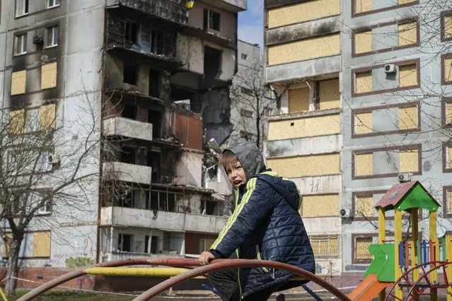 A boy sits on a climbing frame in a playground in front of missile-damaged buildings ahead of a visit by Ukraine's President Volodymyr Zelenskyy in Zaporizhzhia, Ukraine, Monday, March 27, 2023. Zelenskyy has been increasing his travel across Ukraine as his country's war with Russia enters its second year. A team of journalists from The Associated Press traveled with Zelenskyy aboard his train for two nights as he visited troops along the front lines and communities that have been liberated from Russian control. (Photo by Efrem Lukatsky/AP Photo)