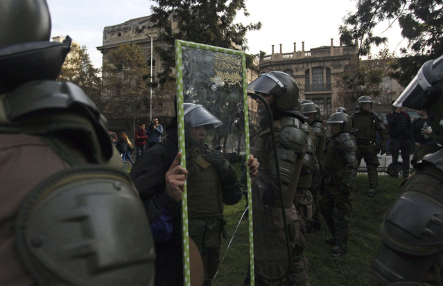 In this Wednesday, May 9, 2018 photo, a demonstrator holds a mirror up to police who detain high school students protesting for higher quality public education, a few blocks from the presidential palace in Santiago, Chile. Students protested near the presidential palace instead of the area far from downtown where the government authorized them to gather. (Photo by Luis Hidalgo/AP Photo)