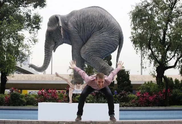 Contemporary French artist Fabien Merelle poses for photos in front of his creation in five meters high sculpture “Pentateuque” in Central, business district of Hong Kong, Tuesday, May 21, 2013. The artwork brings to real life the fantastical and seemingly impossible act of an average man balancing a gigantic elephant. The elephant and the man are modeled on one at the Singapore Zoo and on the artist himself. (Photo by Kin Cheung/AP Photo)