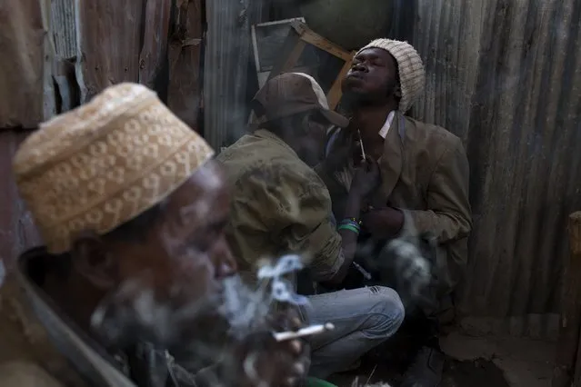 A man smokes a cigarette laced with heroin as Stanley, 36 (C), and Saaid, 32 (R), help each other to inject the drug in Huruma in Nairobi, Kenya, July 6, 2015. (Photo by Siegfried Modola/Reuters)