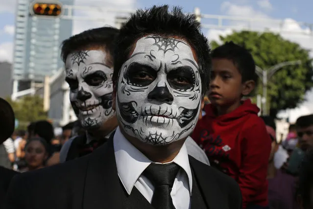 Men with their faces painted as sculls pose for a photo during a Day of the Dead parade along Mexico City's main Reforma Avenue, Saturday, October 29, 2016. Hollywood movies, zombie shows, Halloween and even politics are fast changing Mexico's Day of the Dead celebrations, which traditionally consisted of quiet family gatherings at the graves of their departed loved ones bringing them music, drink and conversation. (Photo by Dario Lopez-Mills/AP Photo)