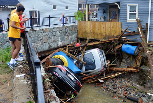 Residents gather by a bridge to look at cars left crumpled in one of the tributaries of the Patapsco River that burst its banks as it channeled through historic Main Street in Ellicott City, Md., Monday, May 28, 2018. Sunday's destructive flooding left the former mill town heartbroken as it had bounded back from another destructive storm less than two years ago. (Photo by David McFadden/AP Photo)