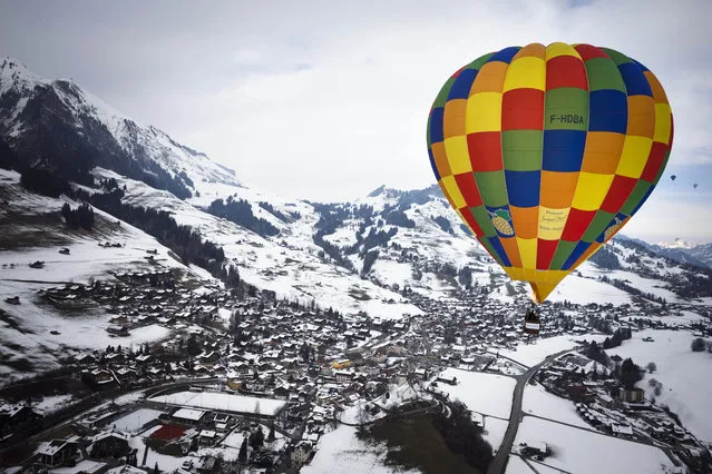 A hot air balloons flies over the snow covered landscape during the 37th International Hot Air Balloon week in the skiing resort of Chateau d'Oex, in the Swiss Alps, Saturday, January 24, 2015. The Swiss mountain resort is famous for ideal flight conditions due to an exceptional microclimate. (Photo by Valentin Flauraud/AP Photo/Keystone)