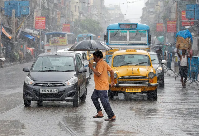 A man carrying an umbrella runs as he crosses a busy road during rain in Kolkata, India, July 10, 2018. (Photo by Rupak De Chowdhuri/Reuters)