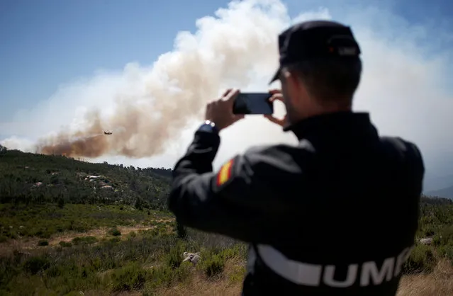 A firefighter films a plane as it drops water on a fire next to the village of Monchique, Portugal August 8, 2018. (Photo by Pedro Nunes/Reuters)
