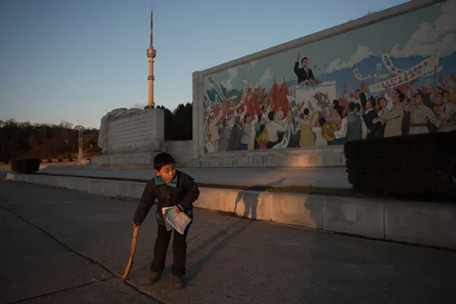 A child sweeps the ground in front of a propaganda mosaic in Pyongyang on December 1, 2016. (Photo by Ed Jones/AFP Photo)