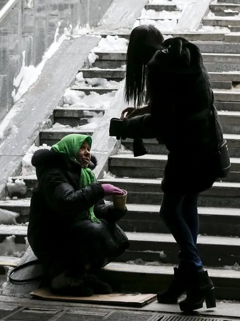 An elderly woman asks for money from a girl in central Kiev, Ukraine, January 18, 2016. Temperatures have plunged to below minus 10 degrees Centegrade and the freezing weather has made life difficult for many older people in Ukraine, many of whose pensions are insufficient to cover heating and food costs. (Photo by Gleb Garanich/Reuters)