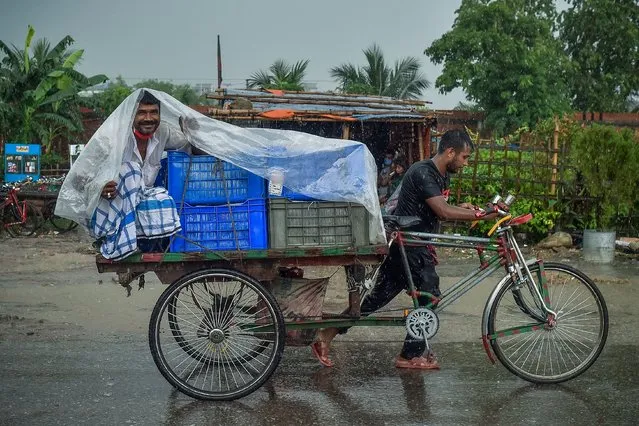 A man wraps a plastic sheet to shelter from the rain while sitting on a cycle-rickshaw cart during a downpour in Dhaka on June 21, 2021. (Photo by Munir Uz Zaman/AFP Photo)