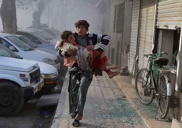 An injured boy carries an injured girl as he runs towards a safe area a few minutes after the suicide bombing in Quetta, Pakistan, Saturday, February 6, 2016. A suicide bomber riding on a bicycle targeted a vehicle carrying security forces in southwestern Pakistan on Saturday, killing some people and wounding many. (Photo by Arshad Butt/AP Photo)