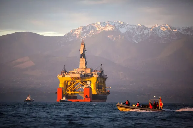 A small boat crosses in front of an oil drilling rig as it arrives aboard a transport ship, following a journey across the Pacific, Friday, April 17, 2015, in view of the Olympic Mountains in Port Angeles, Wash. The 400-foot Polar Pioneer was due to be off-loaded in Port Angeles, on the Olympic Peninsula, to have equipment installed. (Photo by Daniella Beccaria/Seattlepi.com via AP Photo)
