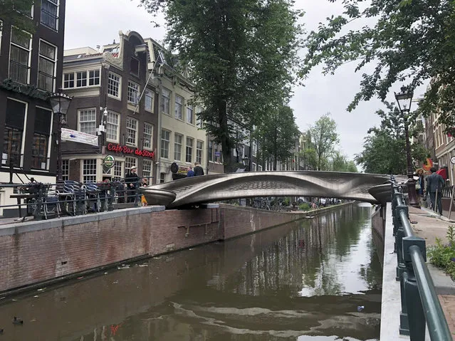 A steel 3D-printed pedestrian bridge spans a canal in the heart of the red light district in Amsterdam, Netherlands, Thursday, July 15, 2021. The distinctive flowing lines of the 12-meter (40-foot) bridge were created using a 3D printing technique called wire and arc additive manufacturing that combines robotics with welding. (Photo by Aleksandar Furtula/AP Photo)