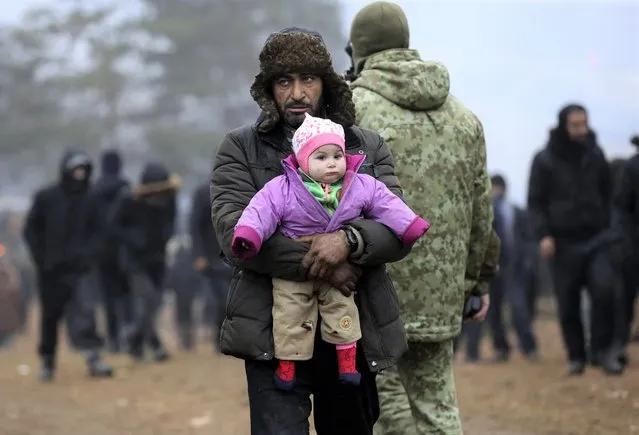 A migrant carrying a child walks in a camp near the Belarusian-Polish border in the Grodno region on November 14, 2021. Dozens of migrants have been detained after crossing into Poland from Belarus, Warsaw said on November 14, warning of a possible larger breakthrough ahead of an EU meeting to widen sanctions on Belarus. (Photo by Oksana Manchuk/BELTA via AFP Photo)