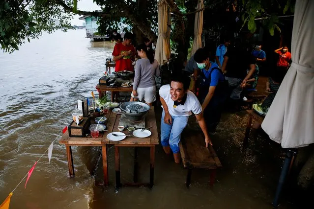 People eat food at a flooded restaurant, where patrons stand up from their tables every time the waves come in, on a river bank in Nonthaburi near Bangkok, Thailand, October 7, 2021. (Photo by Soe Zeya Tun/Reuters)