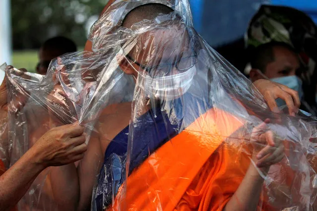A monk covers with himself with a rain poncho in case the police use a water cannon while followers of  Dhammakaya Buddhist temple defied orders to leave its grounds to enable police to seek out their former abbot in Pathum Thani, Thailand February 19, 2017. (Photo by Chaiwat Subprasom/Reuters)