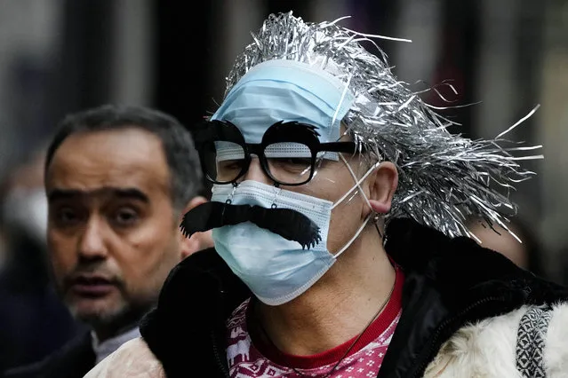 A man wearing face masks with a mustache attached, walks down Regents Street in London, Thursday, December 23, 2021. British Prime Minister Boris Johnson said on Monday that his government reserves the “possibility of taking further action” to protect public health as Omicron spreads across the country. (Photo by Frank Augstein/AP Photo)