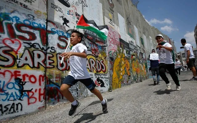 A Palestinian boy runs with his national flag along Israel's controversial separation barrier, which divides the occupied West Bank from Jerusalem, during the “Run for Freedom” marathon in Bethlehem on June 16, 2019, in protest against Trump's expected peace plan proposal. (Photo by Musa Al Shaer/AFP Photo)