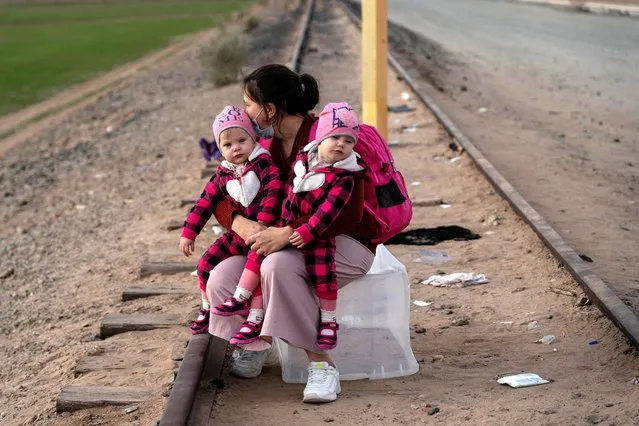 A migrant mother seeking asylum in the U.S. from Ukraine holds her twin daughters near the border fence while waiting to be processed by the U.S. border patrol after crossing the border from Mexico at Yuma, Arizona, U.S., January 22, 2022. (Photo by Go Nakamura/Reuters)